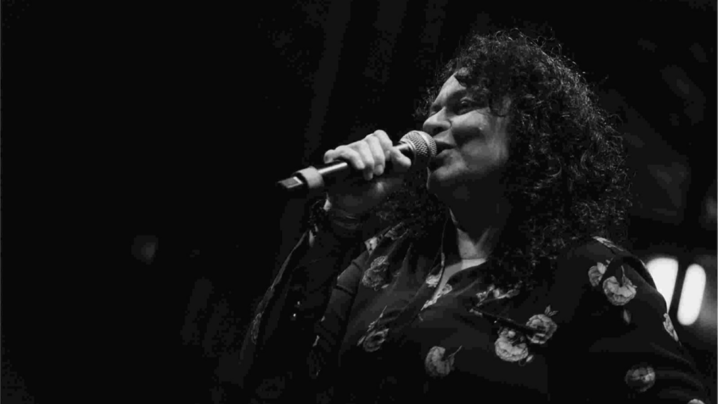 Uma cantora com cabelos cacheados e camisa floral se apresenta com um microfone em uma fotografia artística em preto e branco