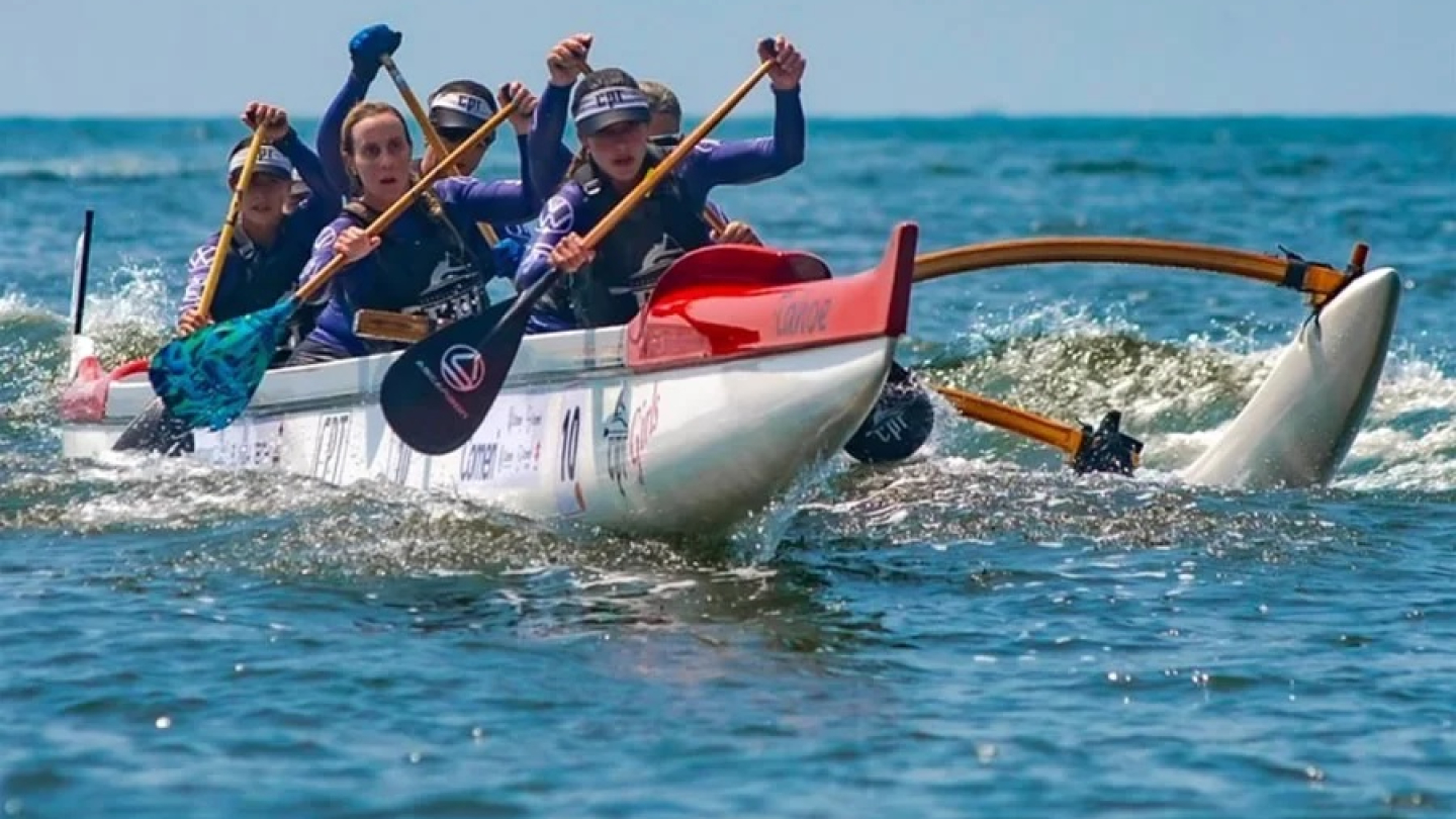 Uma equipe feminina de remadoras em sincronia conduz uma canoa havaiana sobre as águas agitadas do mar