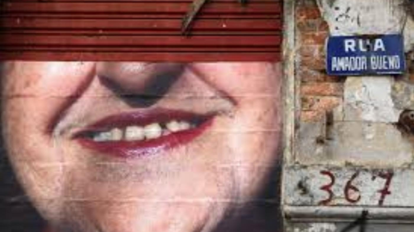 Um mural com o close-up de um rosto sorridente ocupa a fachada de um prédio rústico na Rua Amador Bueno, sob uma porta de enrolar metálica vermelha