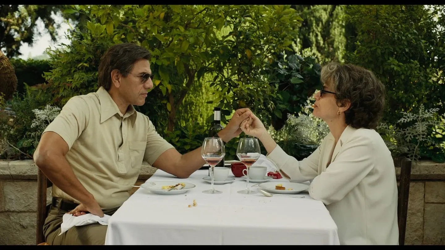 Cena do filme Foi Você Quem Eu Amei, onde um casal compartilha um momento íntimo à mesa em um jardim, segurando as mãos durante uma refeição