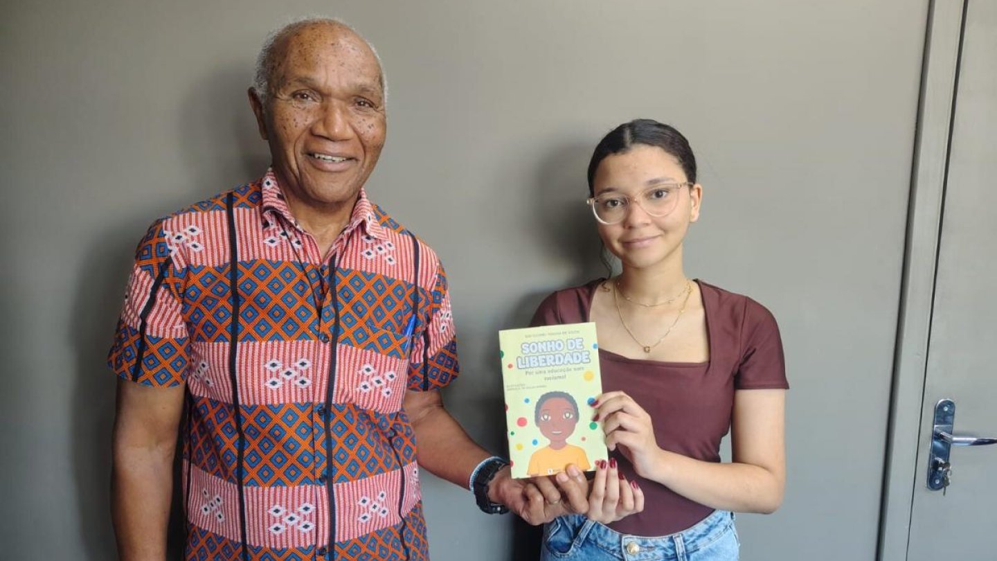 Um homem e uma jovem sorriem para a foto enquanto seguram juntos o livro infantil "Sonho de Liberdade"