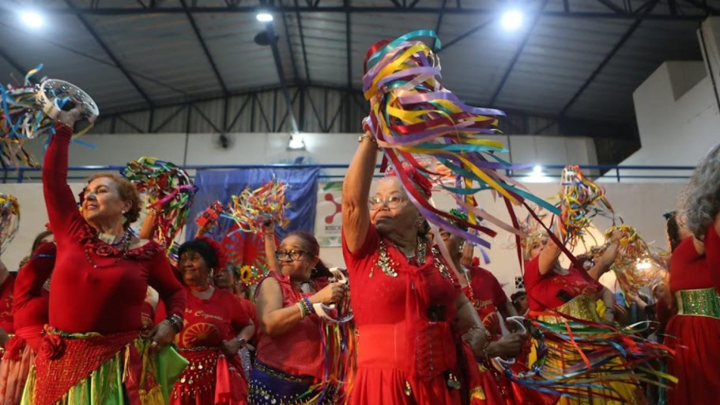 Grupo de mulheres com trajes típicos ciganos vermelhos dançando e celebrando com fitas coloridas e pandeiros em um ambiente festivo