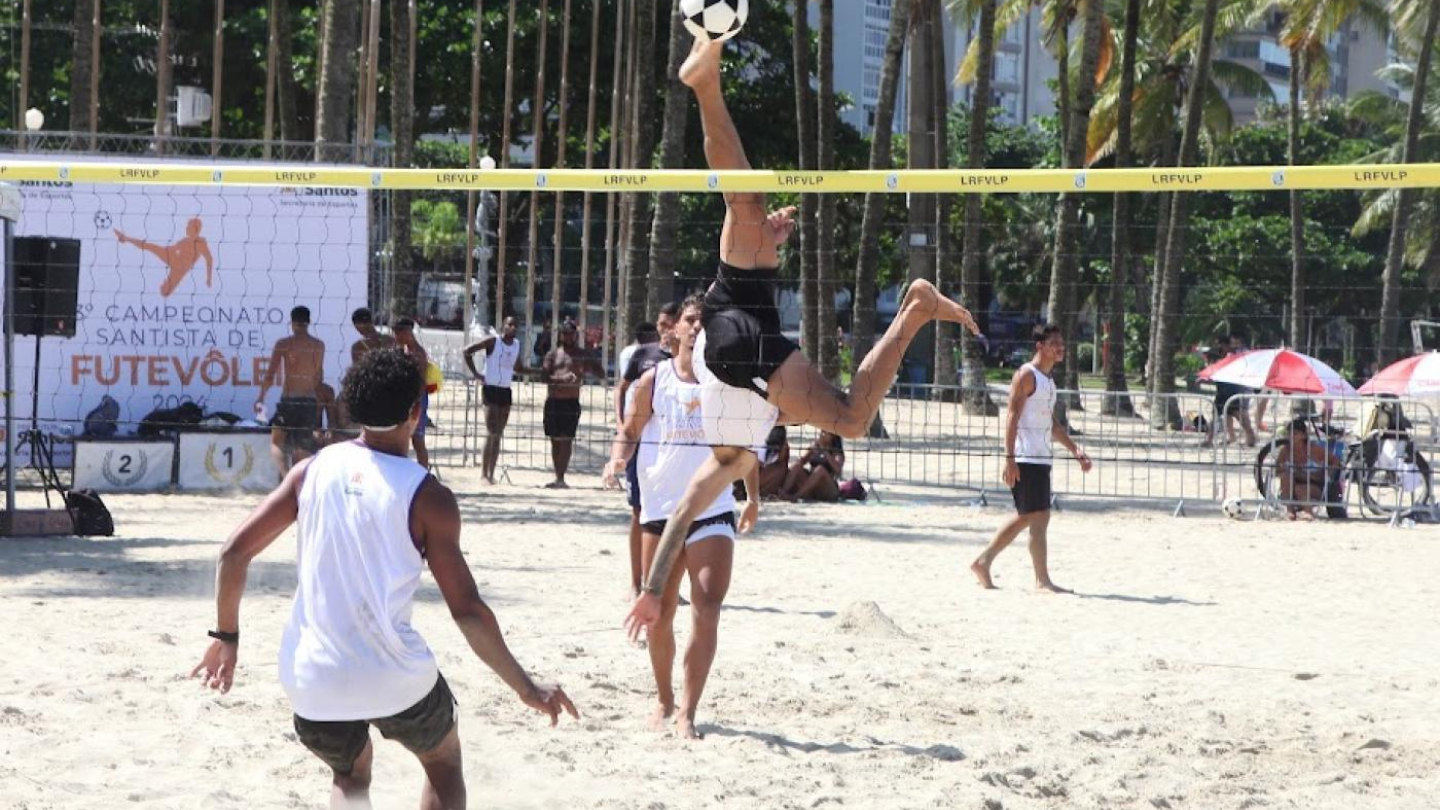Atletas jogam futevôlei na areia da praia num dia ensolarado