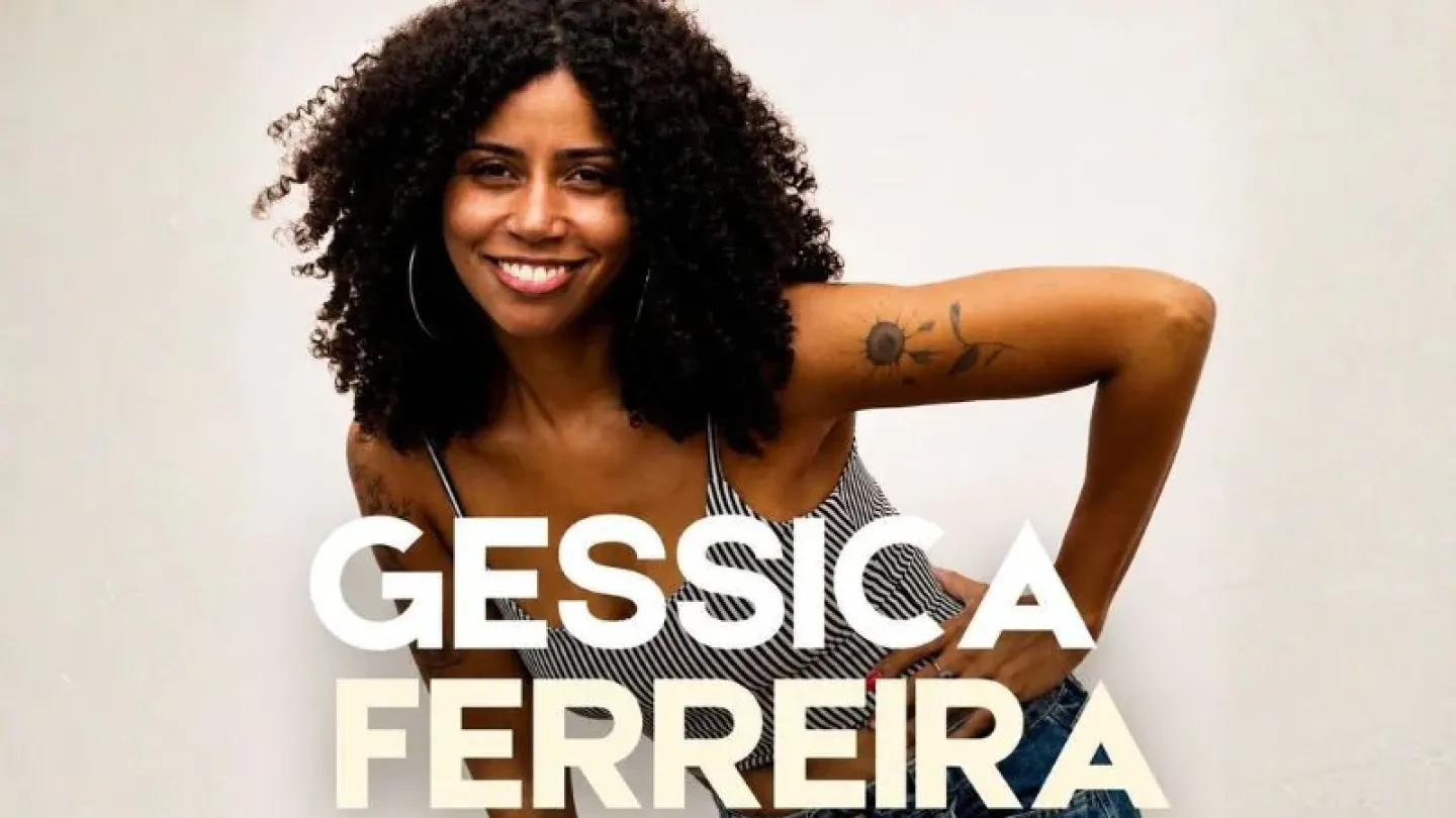 Mulher de cabelos cacheados sorri para a câmera enquanto posa com uma das mãos na cintura. Ela veste blusa listrada sem mangas e calça jeans azul. Ao centro da imagem, aparece o nome "Gessica Ferreira" em letras brancas.