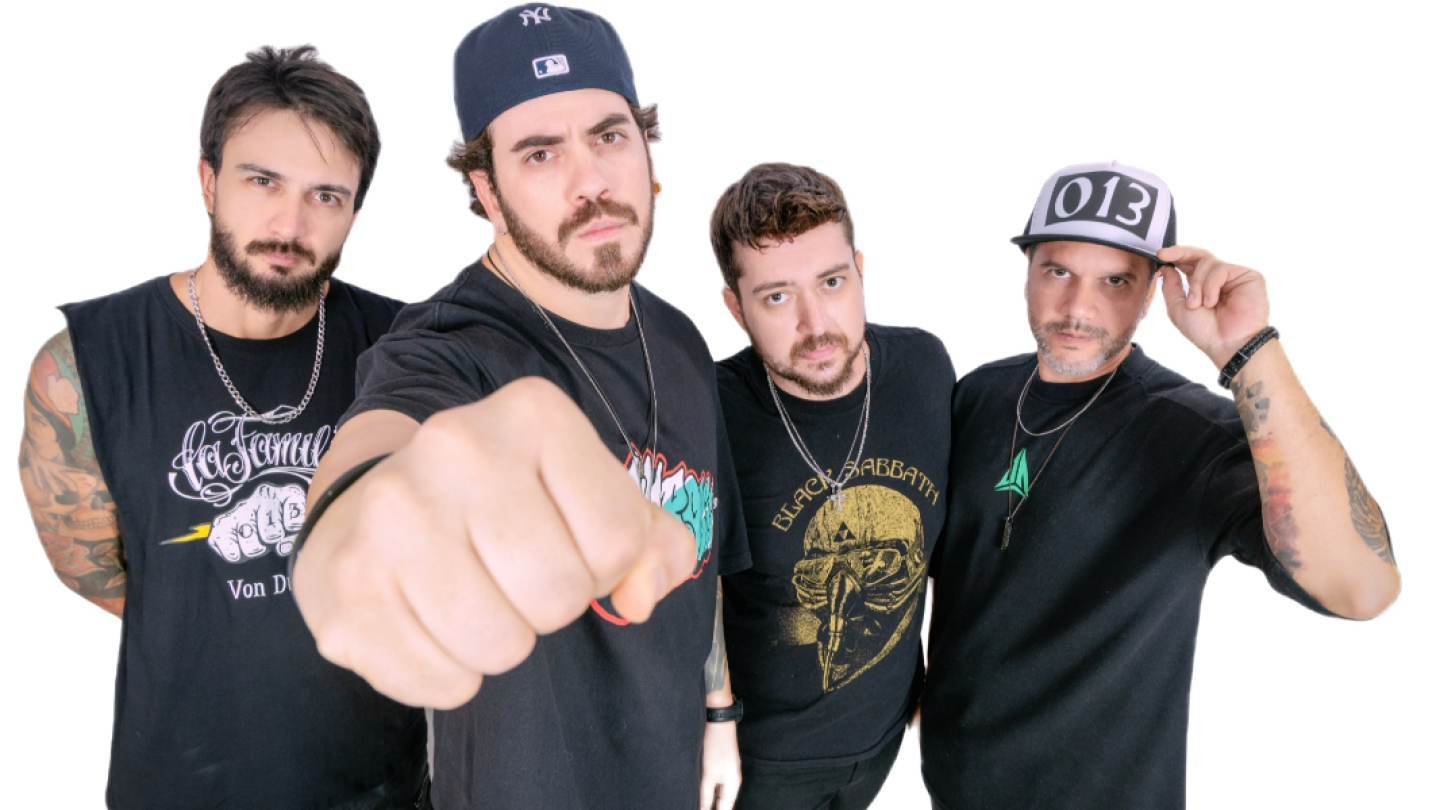 Fotografia promocional de uma banda formada por quatro integrantes diante de um fundo branco. Todos vestem roupas pretas em estilo casual, com camisetas de bandas e acessórios como correntes e bonés. O integrante ao centro aparece em primeiro plano com o punho cerrado em direção à câmera, criando um efeito de perspectiva e transmitindo atitude e energia. Os demais músicos posam com expressões sérias, enquanto um deles ajusta o boné. A composição reforça a identidade do grupo e remete ao universo do rock e d