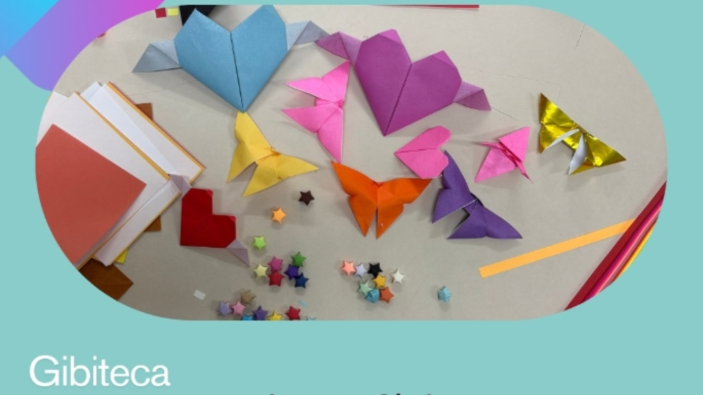 Card de divulgação da Gibiteca de Santos com uma mesa repleta de dobraduras de origami coloridas, incluindo corações, borboletas, pássaros e estrelas de papel. O fundo é azul-claro com elementos gráficos e um ícone de origami. O texto destaca um evento especial de férias com oficina de origami e feira de troca de histórias em quadrinhos. No canto inferior direito está a logomarca da Secretaria de Cultura de Santos.